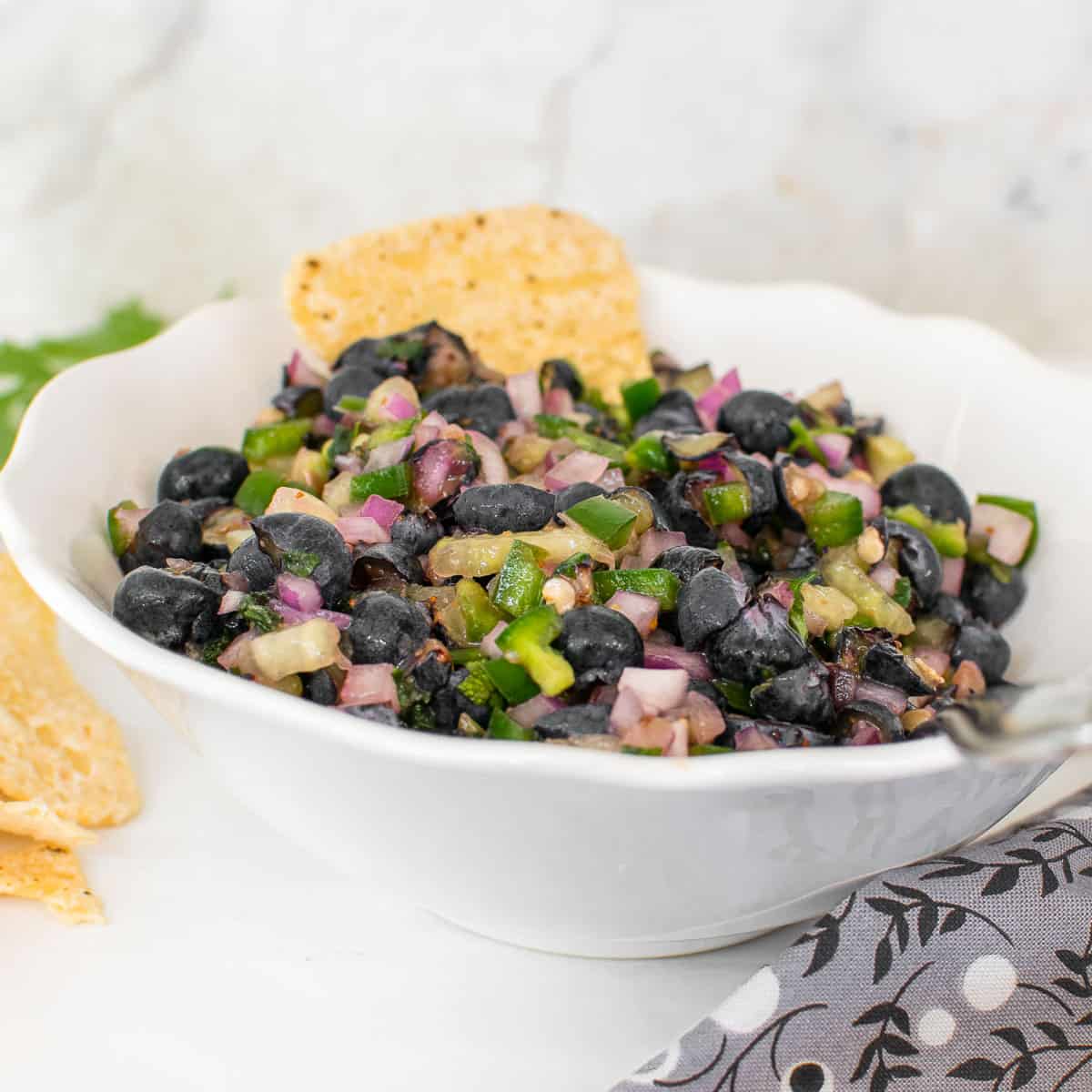 a front view of blueberry salsa in a serving bowl with a chip dipped in it. 