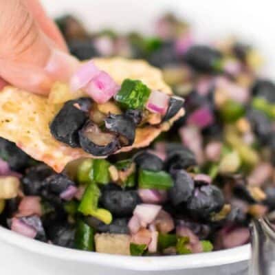 a hand holding a chip with blueberry salsa on it.