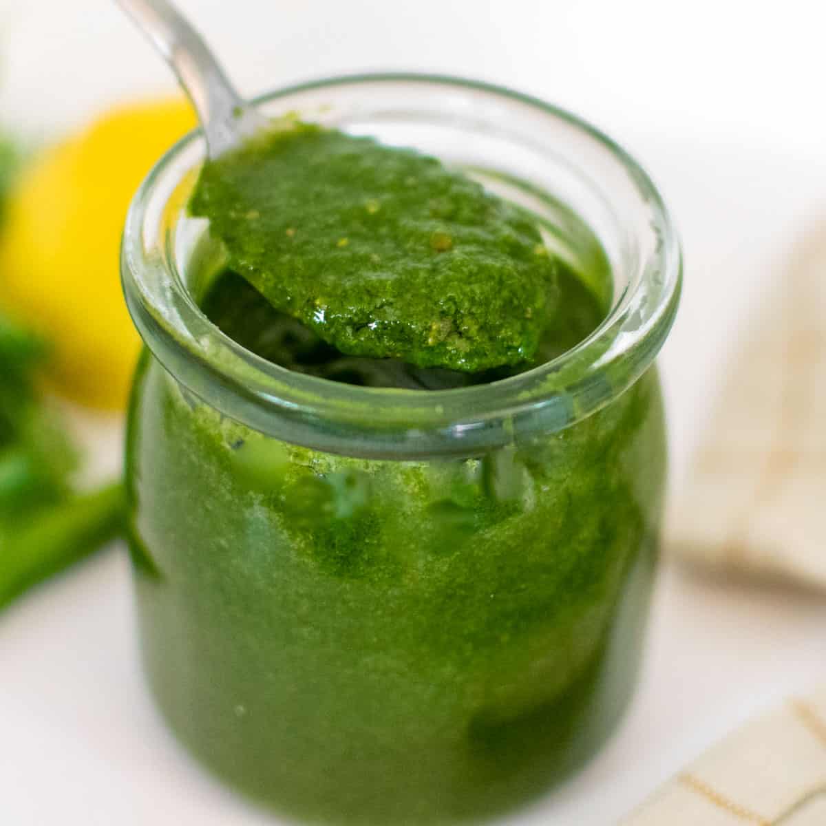 a spoon picking up cilantro chutney from the jar.