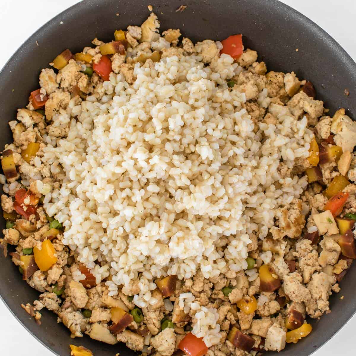 cooked brown rice folded in the pan with other ingredients.