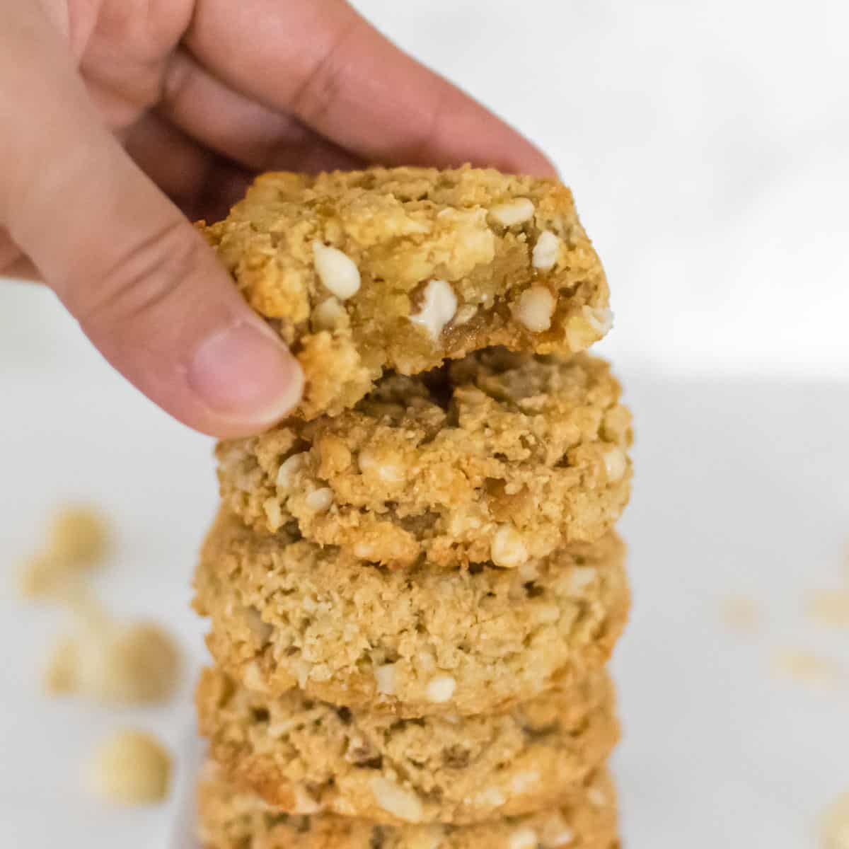 a hand placing half eaten macadamia nut cookie on its stack. 