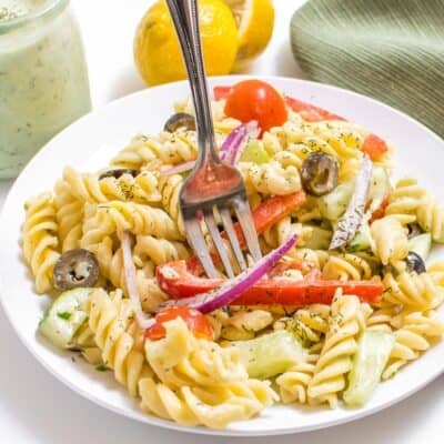 a fork digging into a plate full of tzatziki pasta salad.