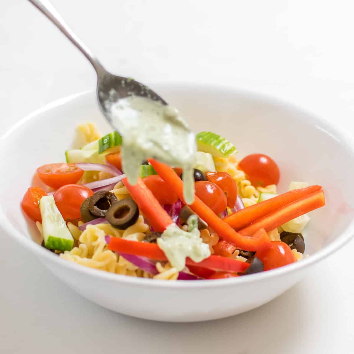 a spoon drizzling the dressing over the veggies.