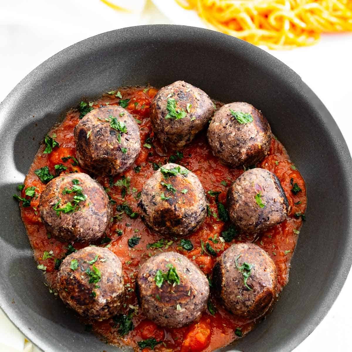 top view of black bean meatballs in a pan with sauce and pasta on the side.