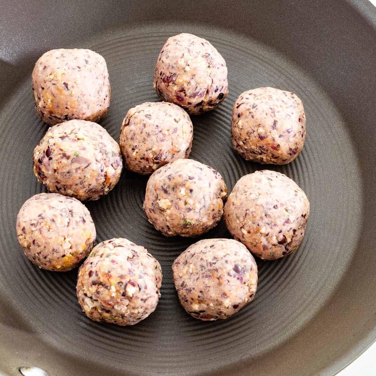 shaped meatballs in the a pan ready to be cooked. 