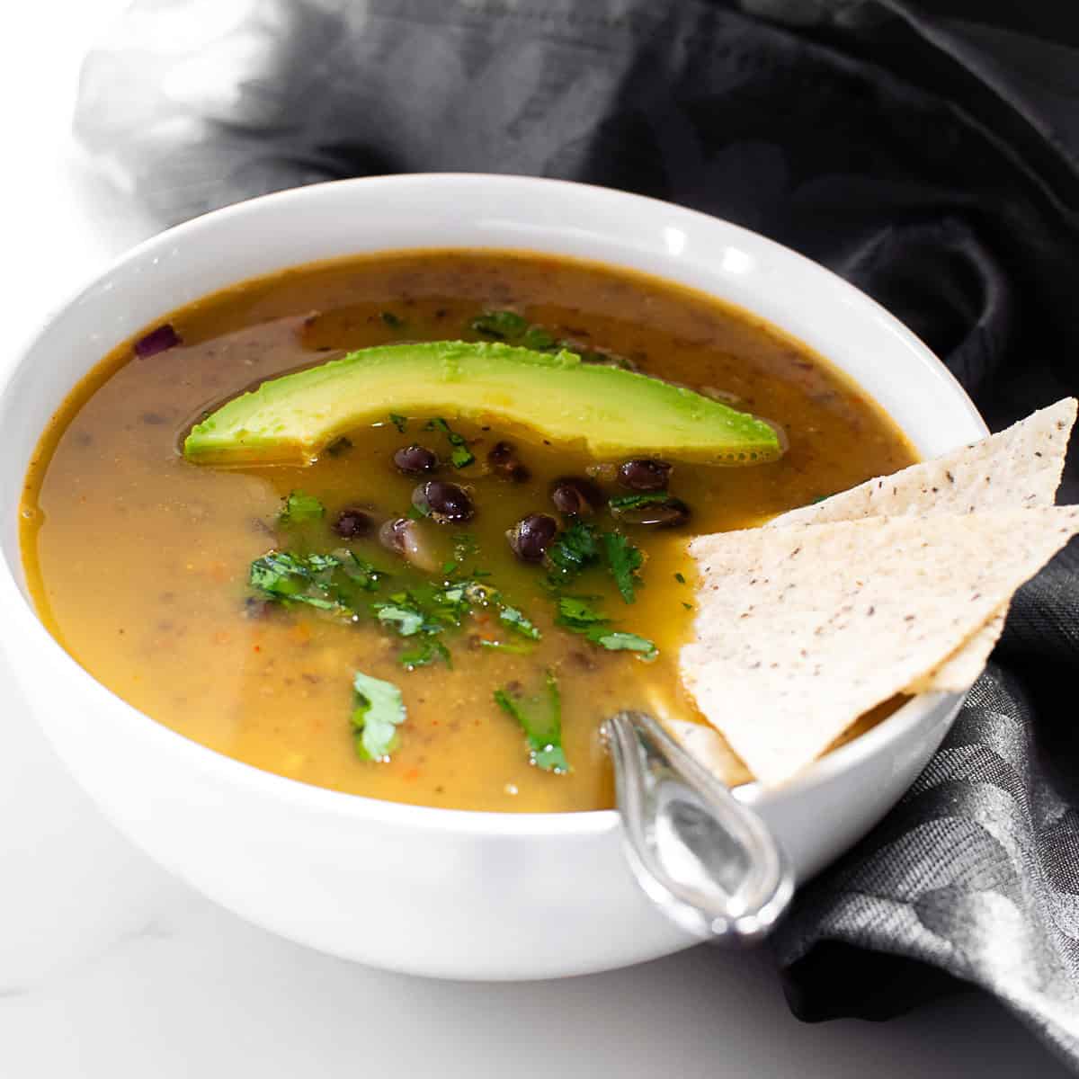 a 45 degree angle view of black bean soup in a bowl with garnishes. 