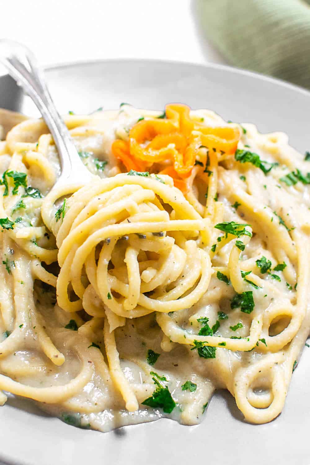 Close up view of a fork twirled with cauliflower alfredo sauce pasta.