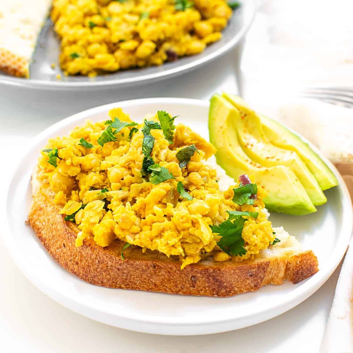 chickpea scramble on a slice of toast with avocado on the side.