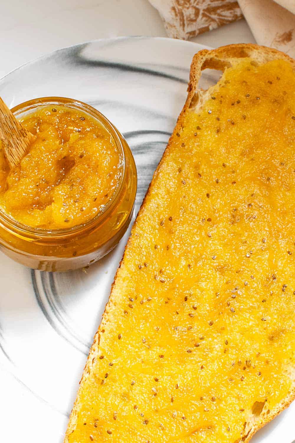 top view of a toast slathered with jam with a jar of pineapple jam on the side.