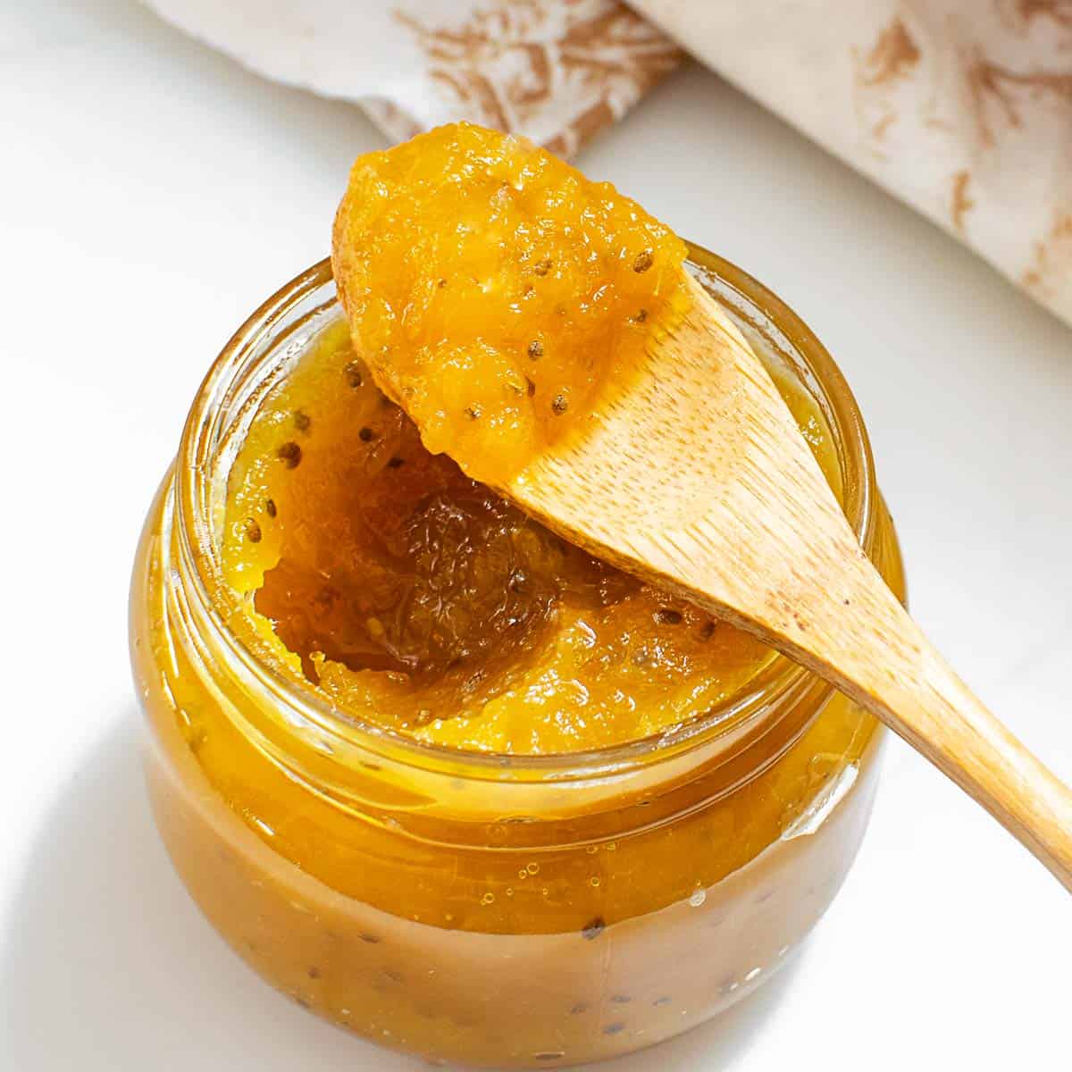 a spoon with pineapple jam resting on top of its jar.