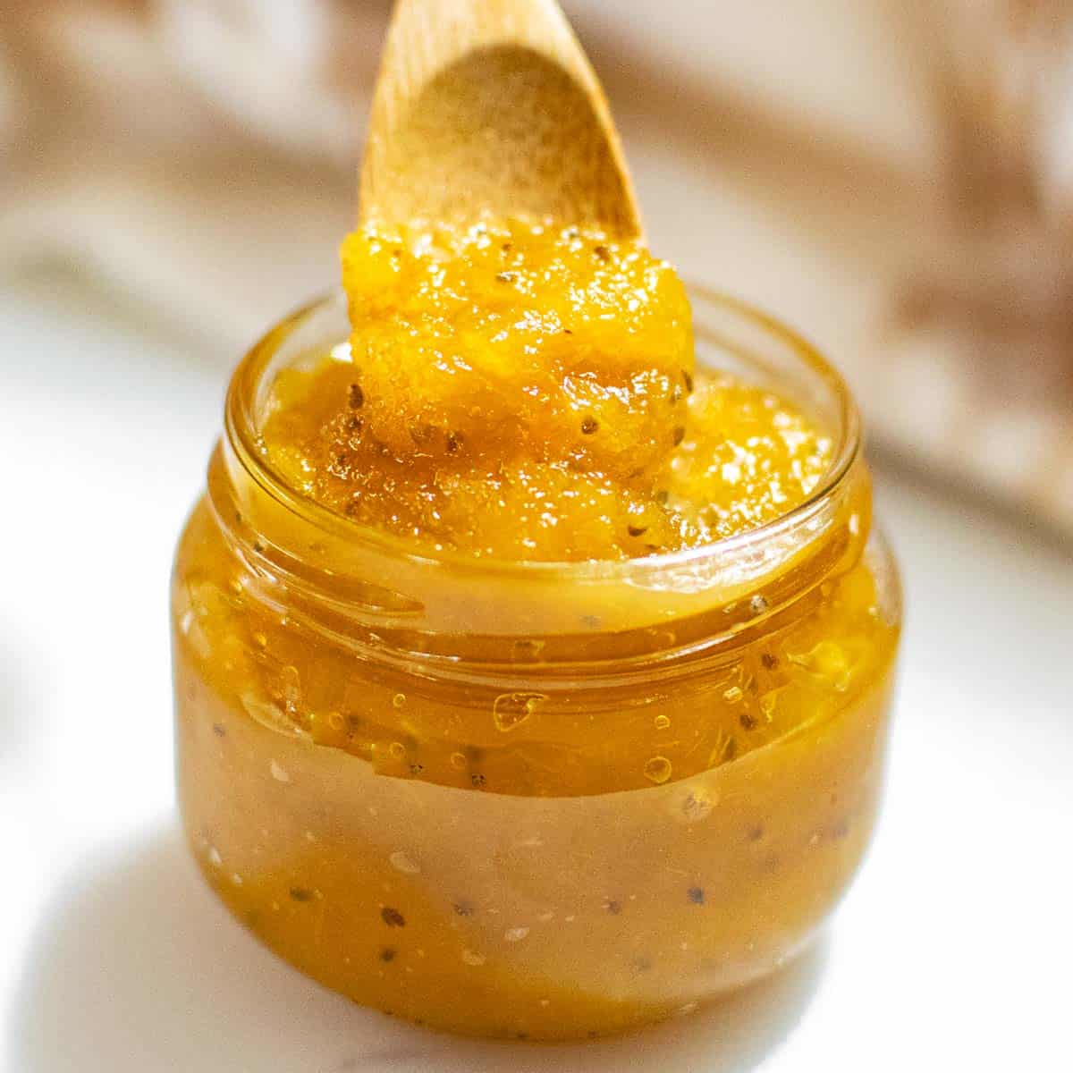 a spoon pouring pineapple jam into the glass jar.