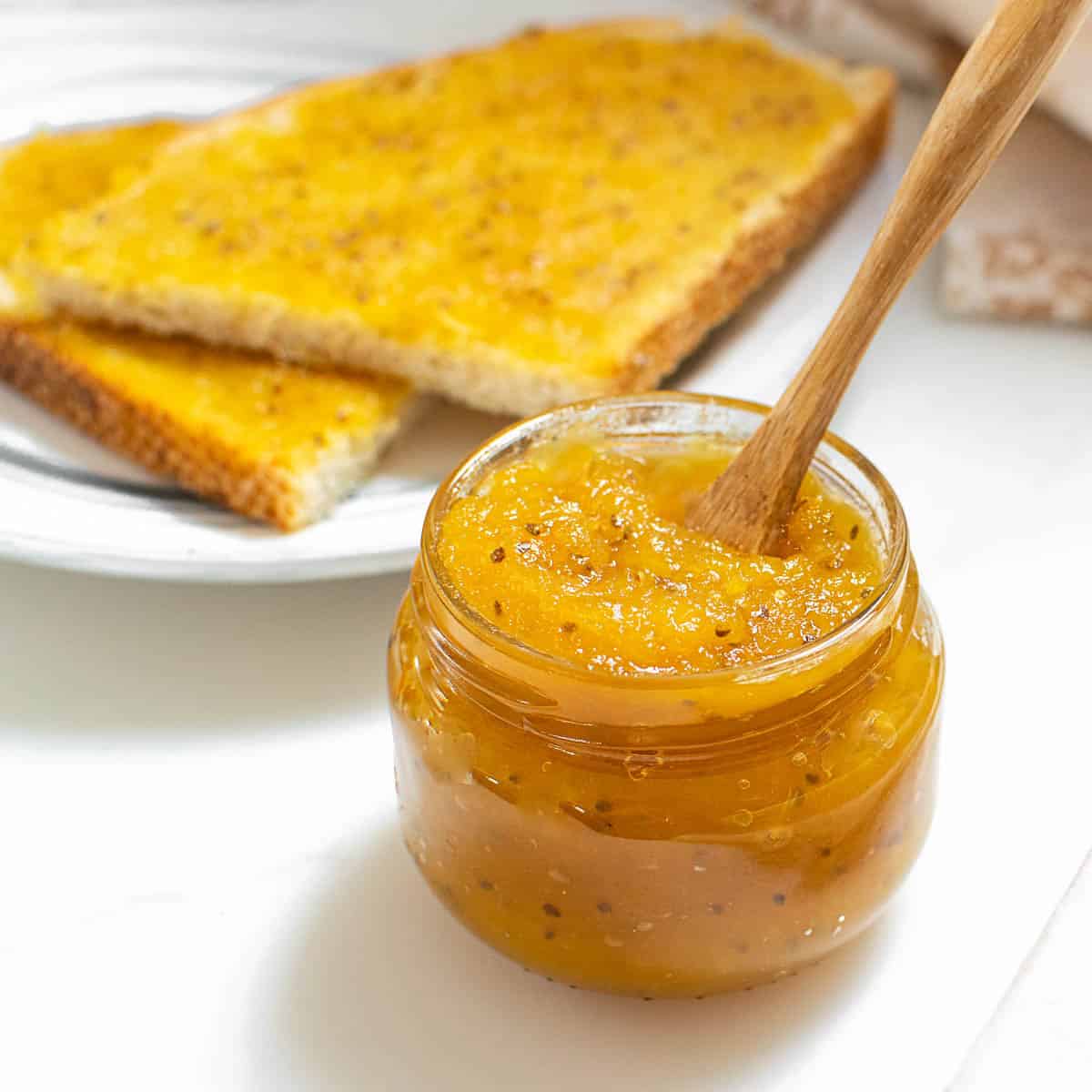 a glass jar of pineapple jam with jam toast at the background.
