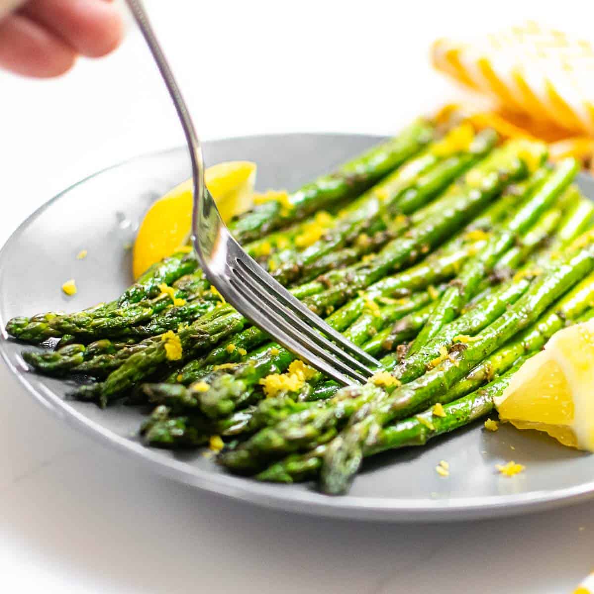 a fork digging into cooked asparagus served on a plate.