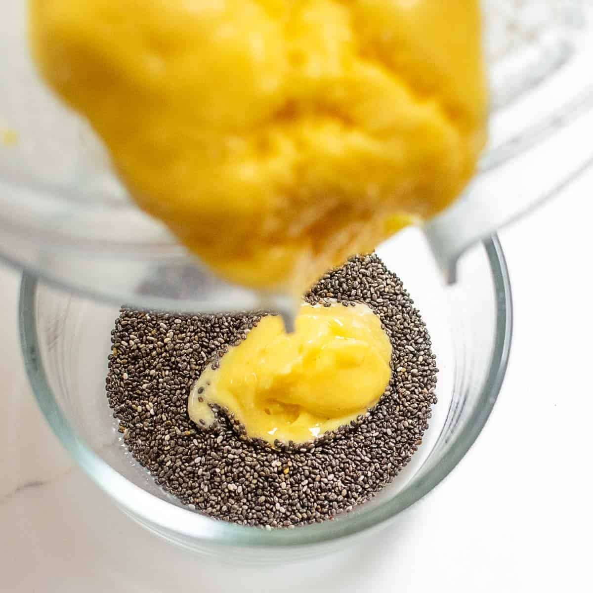 mango puree being poured into the bowl of chia seeds.
