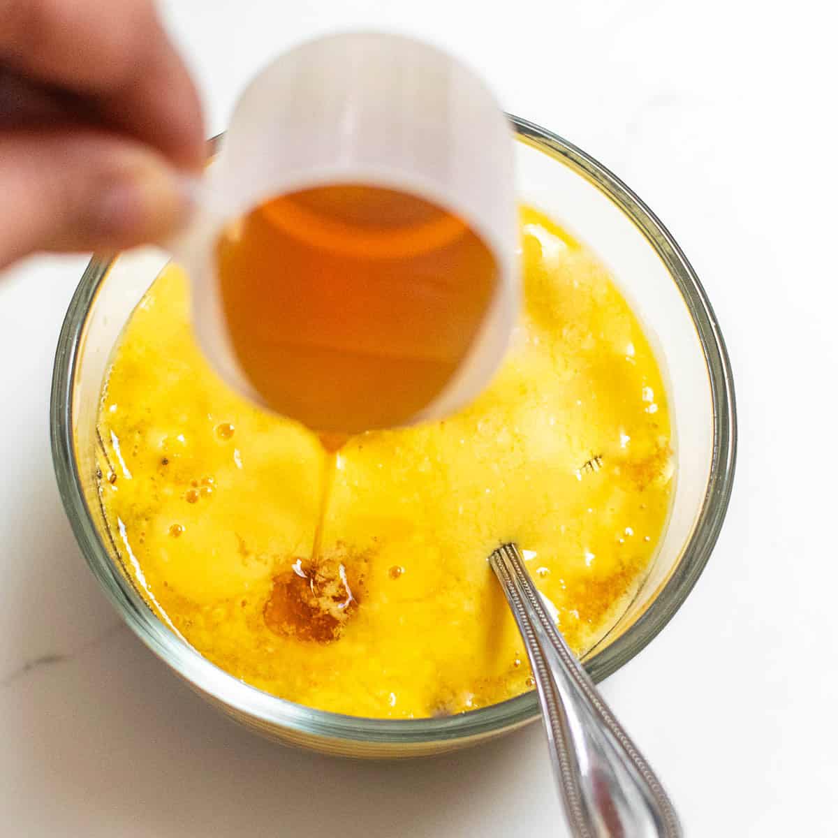 a hand holding the maple syrup cup and pouring into the bowl. 