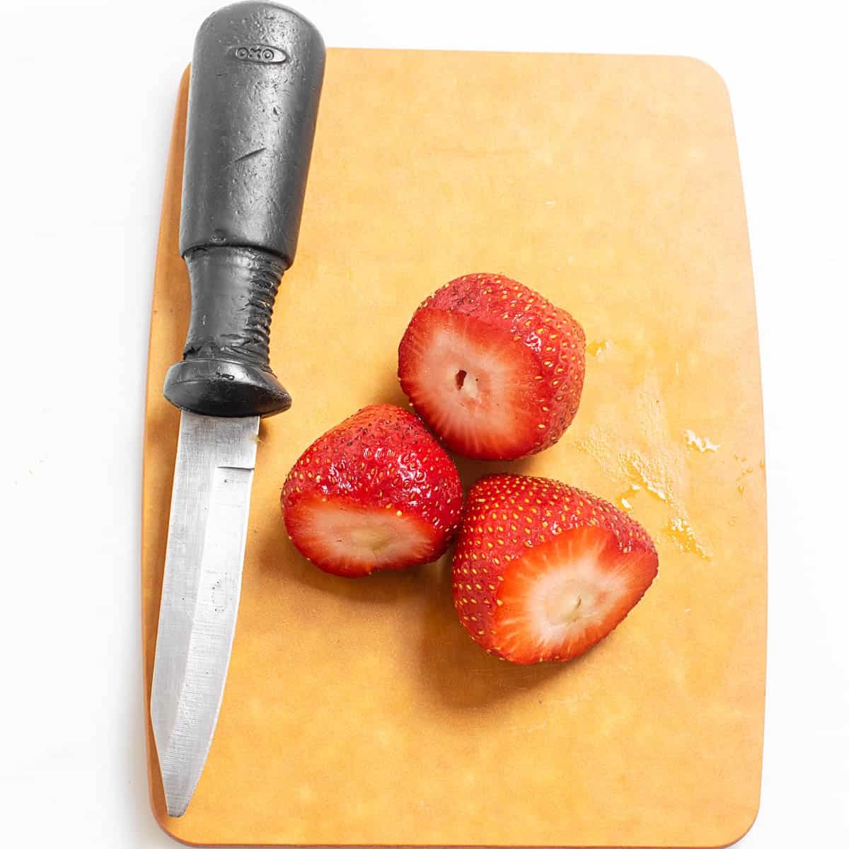 hulled strawberries with a knife on a wooden cutting board.