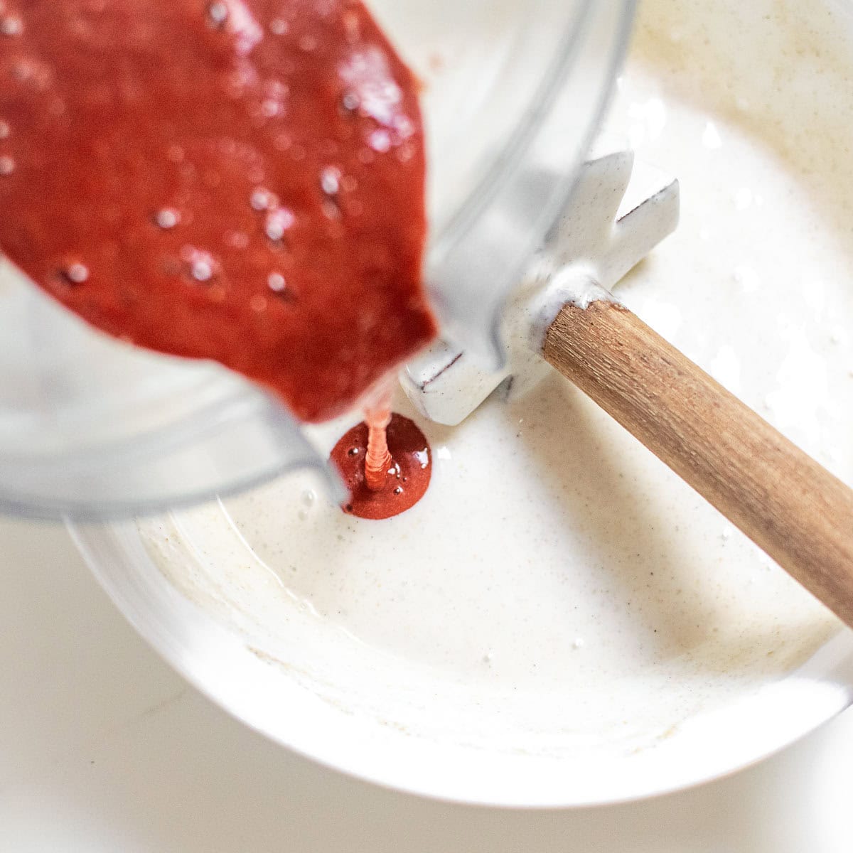 strawberry mixture being poured from a blender into the bowl of yogurt mixture. 